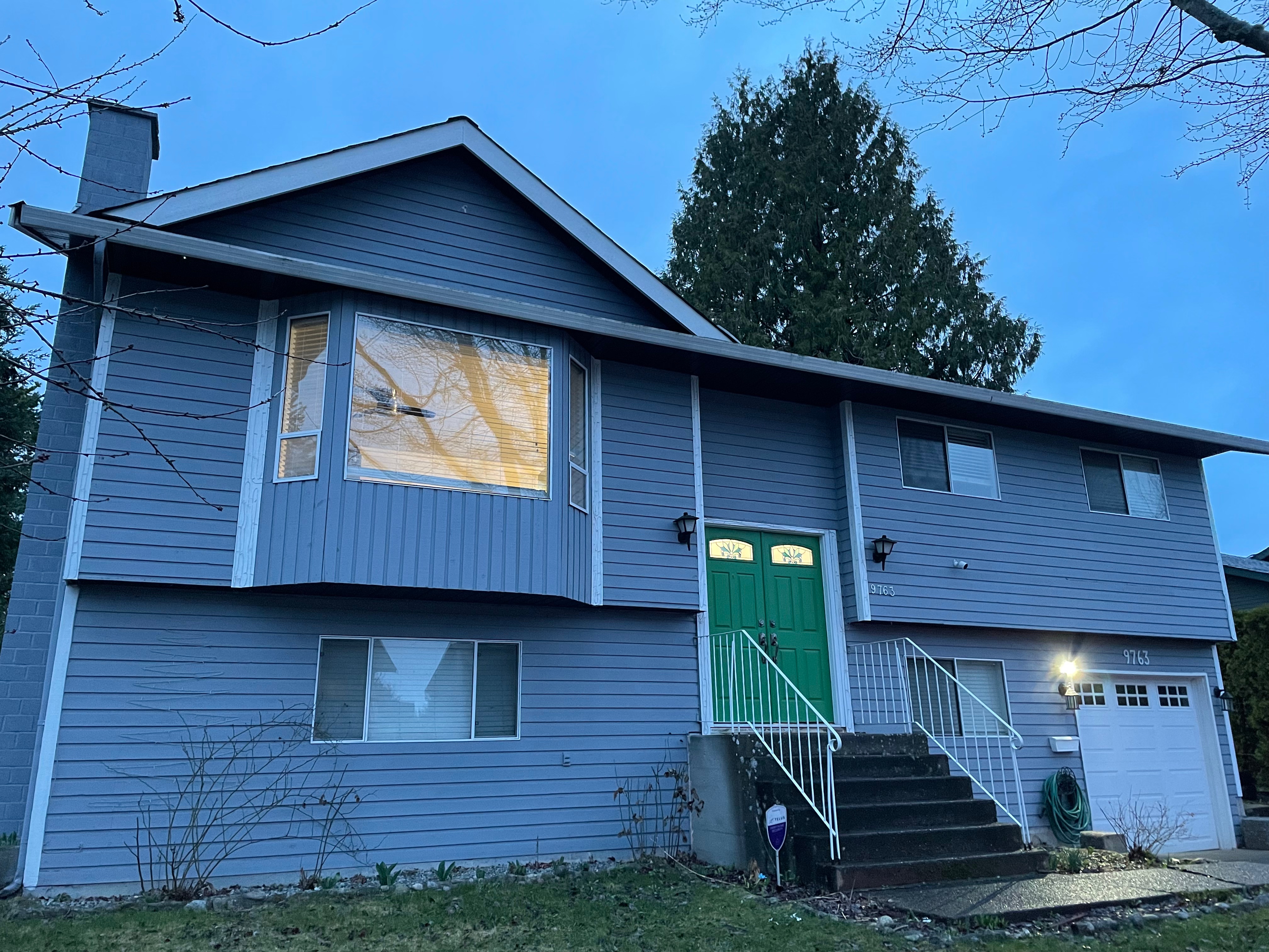 Exterior view of a blue two-story house featuring a green front door, large windows, and outdoor stairs.